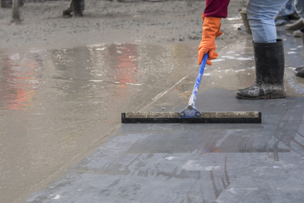 Construction worker troweling wet concrete on a top of concrete